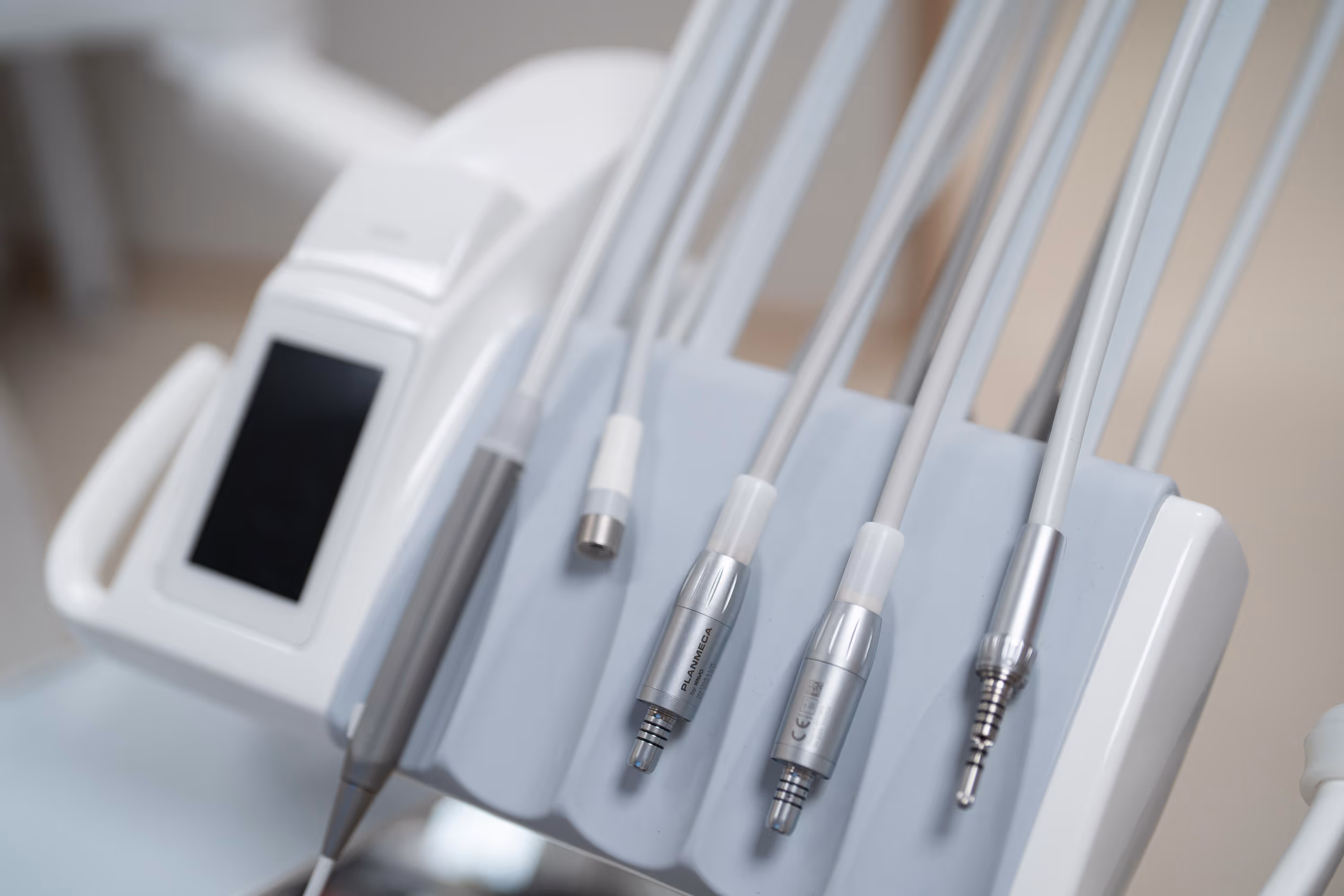 Hammaslääkärin tuolin instrumentit, harmaat letkut ja metalliset kärjet, valkoinen tuoli, kirkas valaistus.